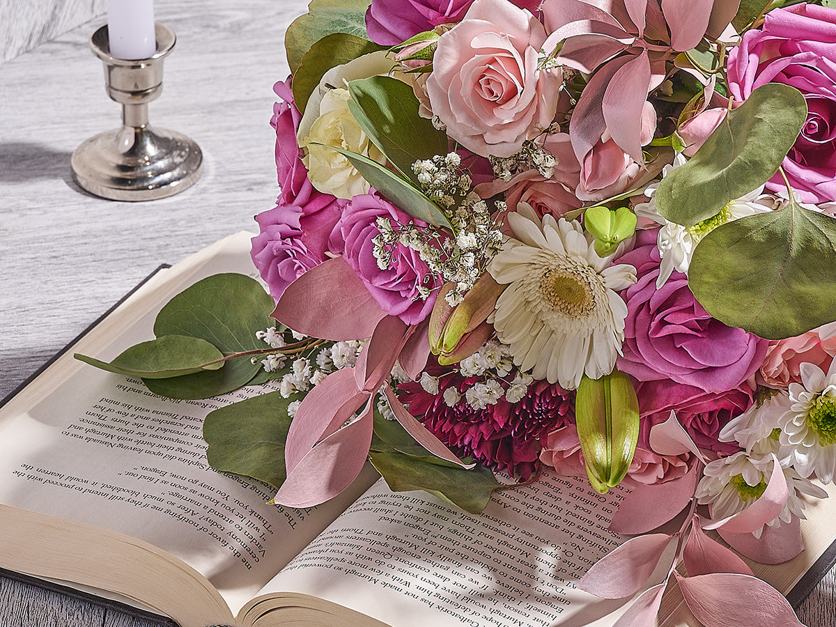 Bouquet of pink and green flowers on an open book with a candle in the background