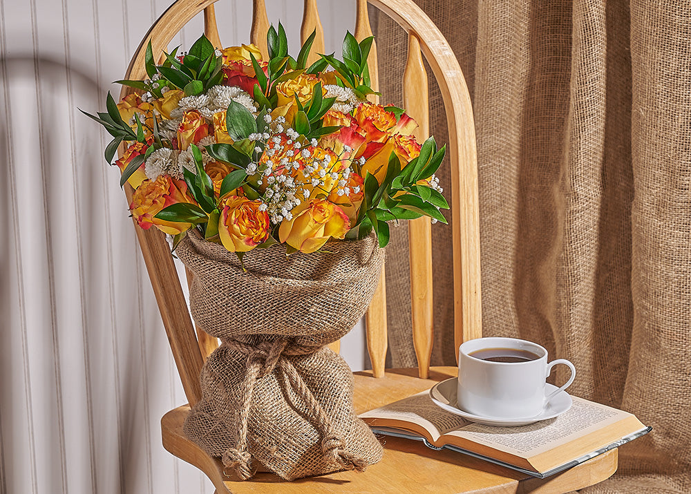 Bouquet of flowers in burlap on a wooden chair with a cup of coffee and book.
